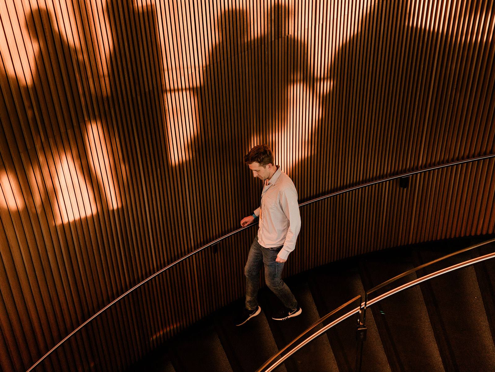 Brian Houck walking down a curved staircase beside a sunlit wooden wall.
